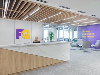 Woman sitting at a front desk. Large desk that is made of half wood and half marble material. Circle of chairs.